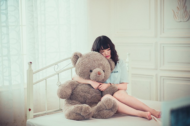 Žena s veľkým plyšovým medveďom sediaca na posteli.jpg