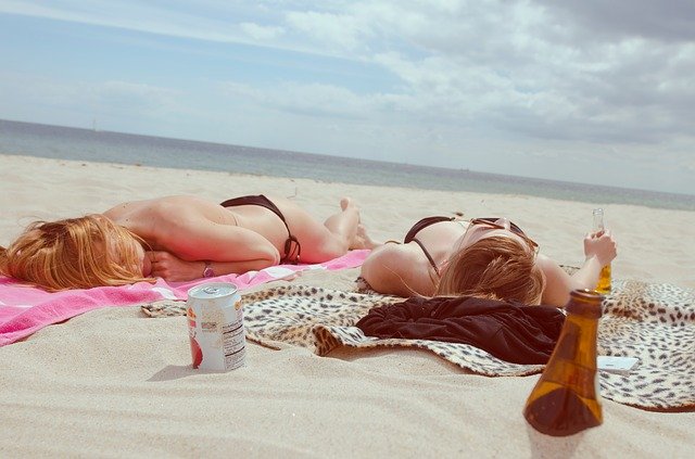 Dve ženy v plavkách sa opaľujú na uteráku na pieskovej pláži.jpg